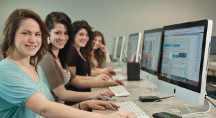 Quatre étudiantes travaillent à des projets de design graphique, à un ordinateur.